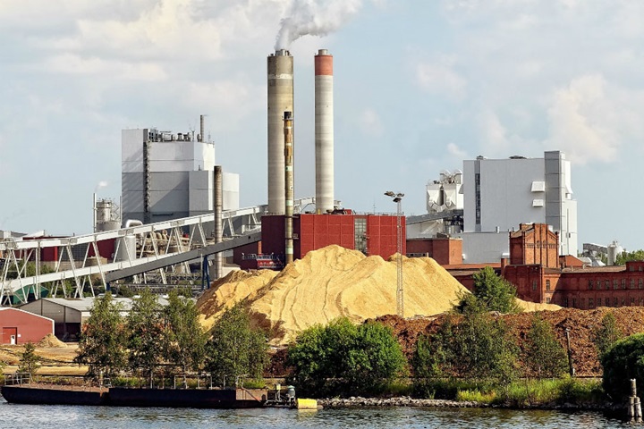 Riverfront paper mill with large wood chip storage pile