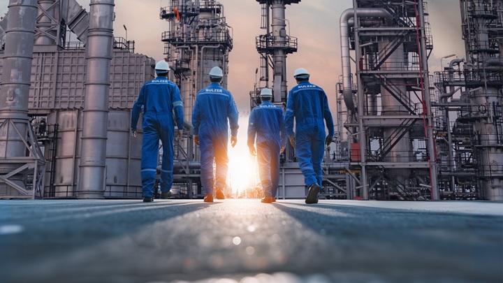 Sulzer technicians walking toward an industrial plant to perform maintenance tower services